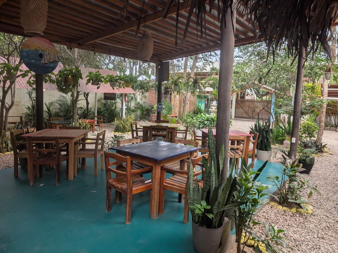 The Surfing Cowboy's covered patio, with wooden tables set among palms and potted plants