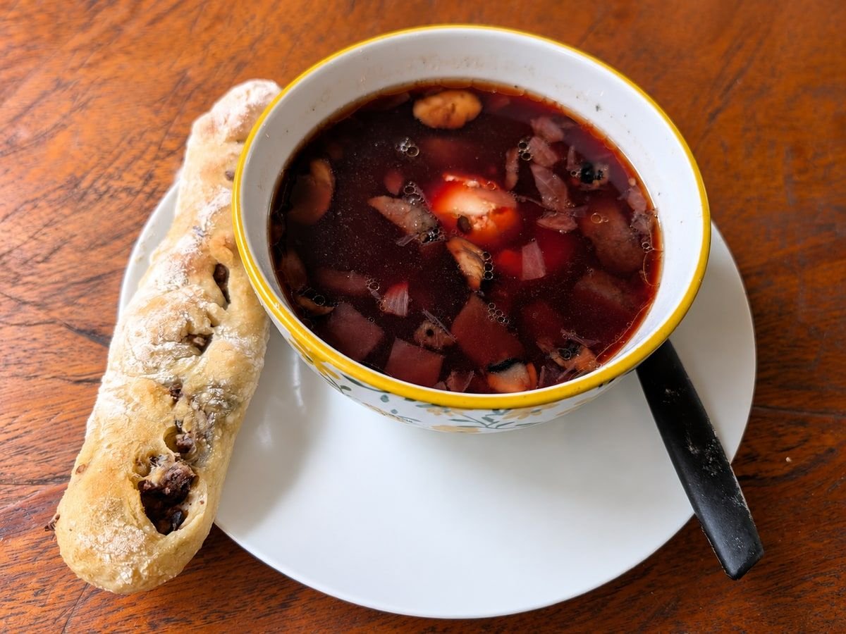 Red beet soup in a yellow-rimmed bowl beside a homemade meat croquette