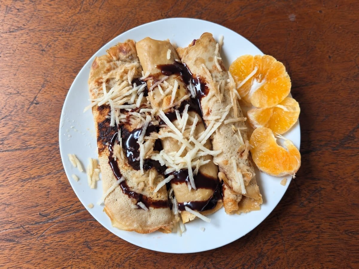 Folded crêpes with dark sauce and a shredded topping, served with orange slices