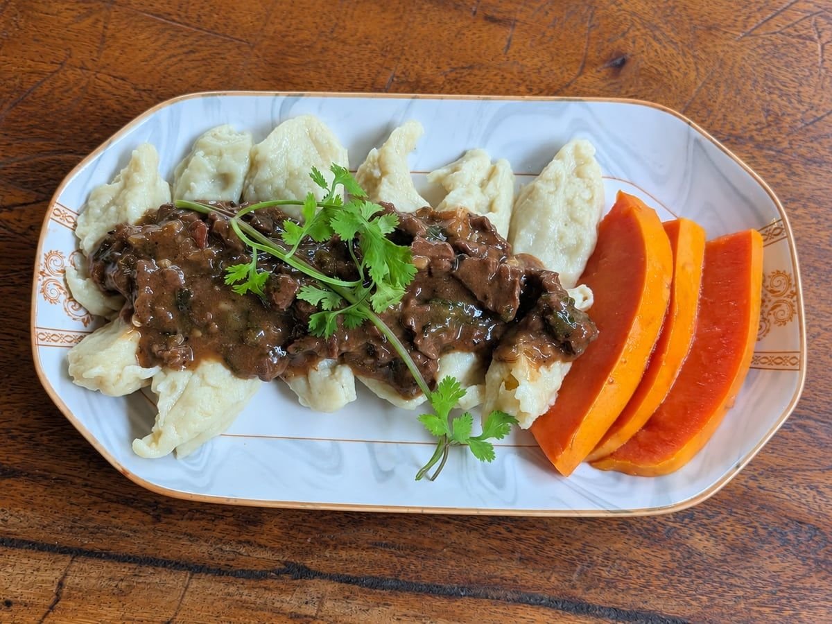 Potato dumplings topped with beef and cilantro on a rectangular plate