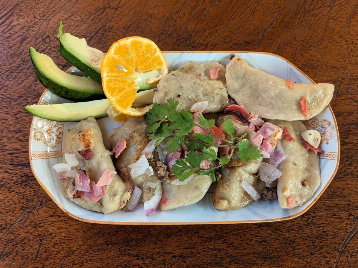 Meat pierogies topped with onions and cilantro, with avocado and orange slices