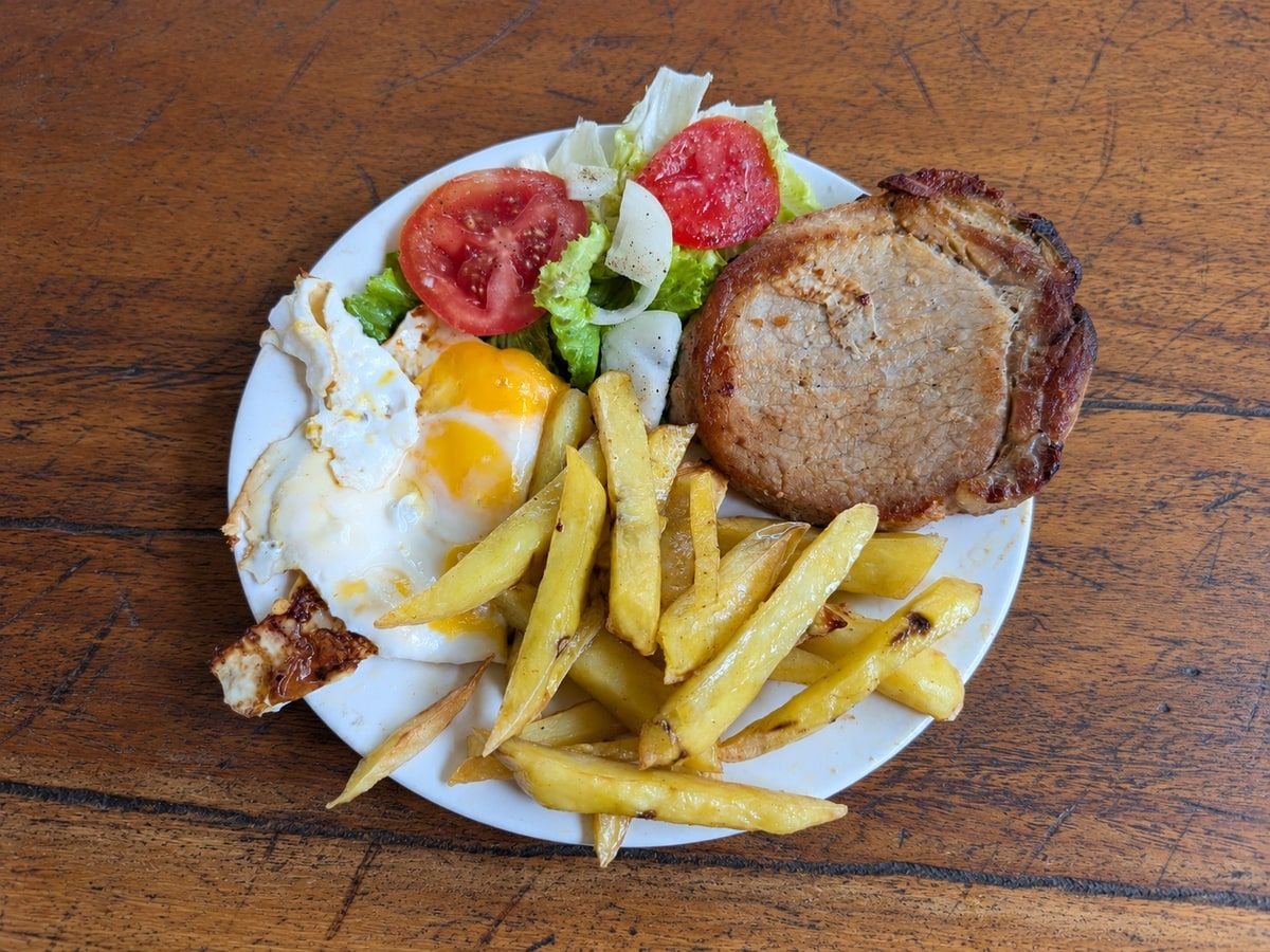 Two fried eggs with a pork chop, French fries, lettuce, tomatoes, and onion on a white plate