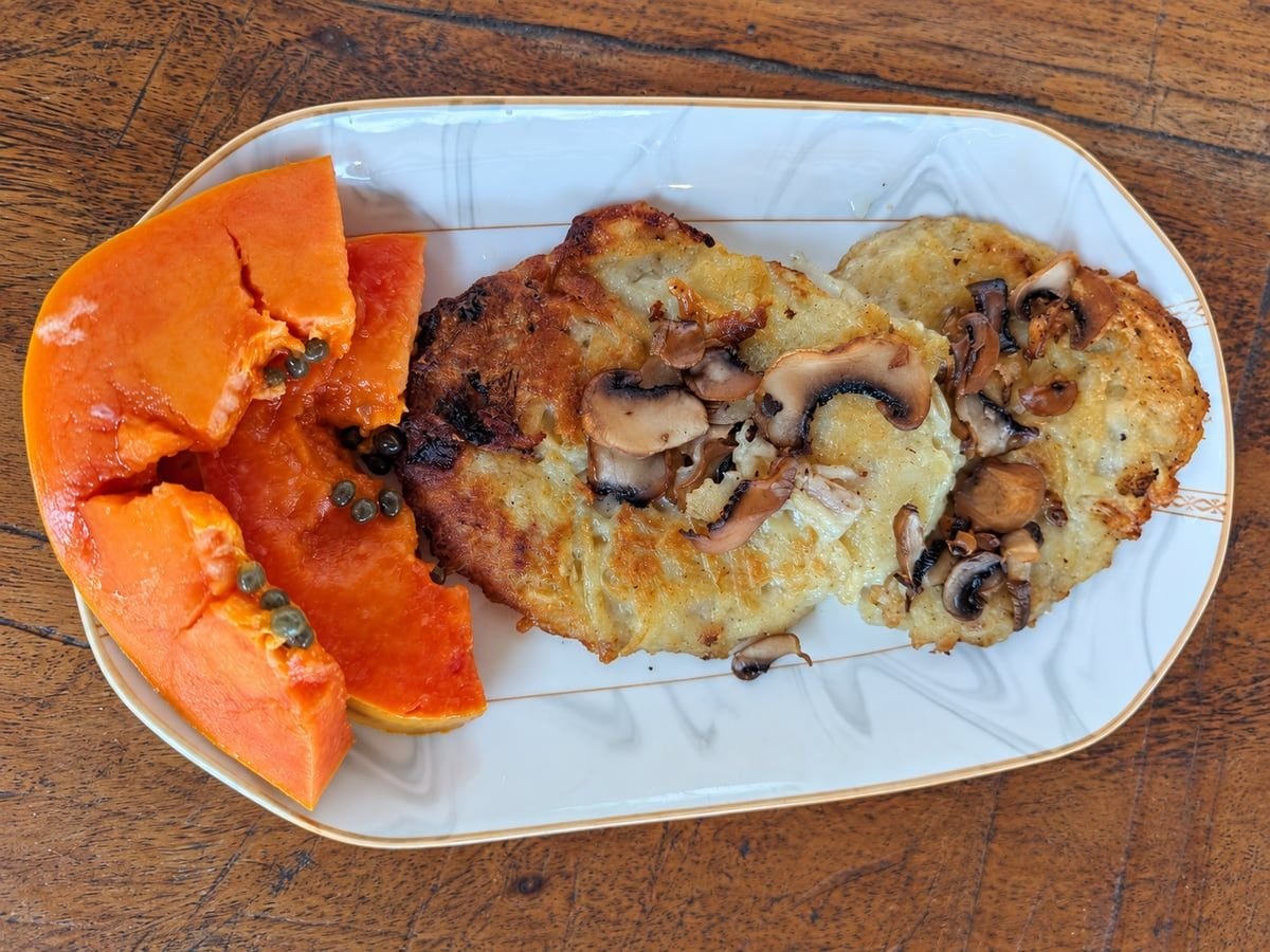 Golden potato pancakes topped with mushrooms beside papaya slices