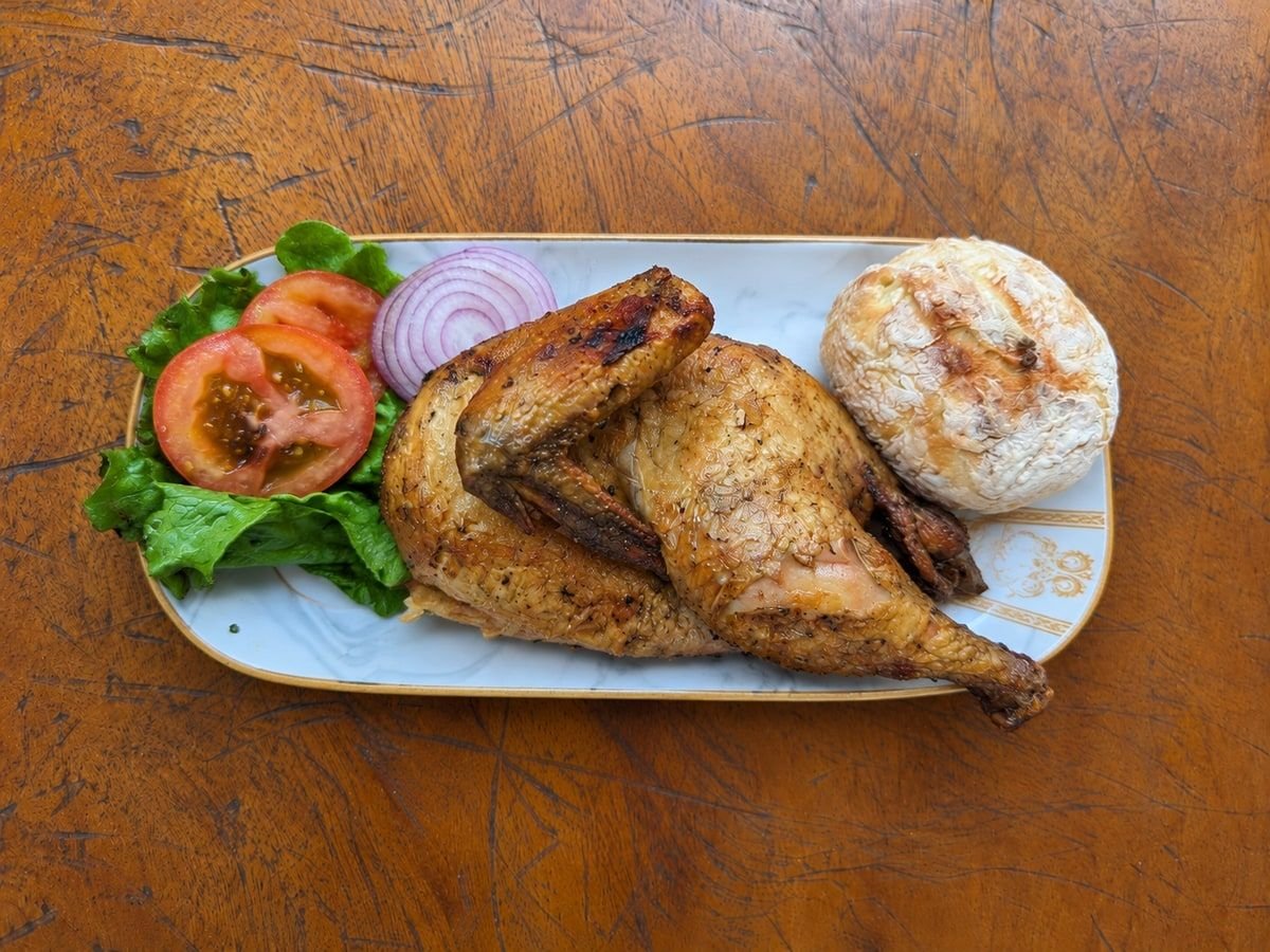 Roasted half chicken with homemade bread, lettuce, tomatoes, and red onion on a rectangular plate